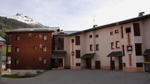 A building with a central courtyard, featuring a mix of wooden and beige facades, and a mountain backdrop.