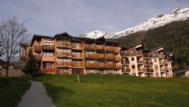 A multi-story hotel with balconies, a paved pathway, and a mountainous backdrop.
