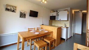 A compact kitchen with a wooden table and chairs, a microwave, and a TV on the wall.