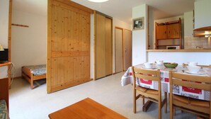 A cozy room with a wooden bed, a small desk, a dining table with chairs, and a kitchen area with cabinets and a hanging light fixture. - 10m from ski slopes, 2nd floor, balcony, tv, ski locker, 27m², Val Cenis (Termignon)