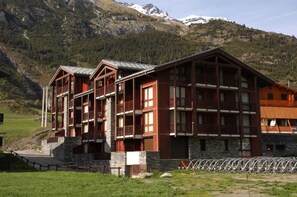 Um edifício com várias andares e varandas, com montanhas ao fundo.