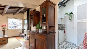 A traditional kitchen with wooden cabinets, a tiled floor, and a window with a view of buildings.