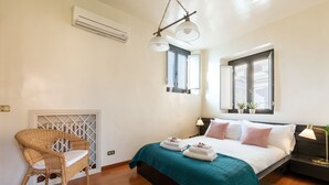 A bedroom with a bed, a chair, a window, and an air conditioning unit.