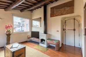 A cozy living room with a fireplace, wooden flooring, a large window, and a painting on the wall. - Rome As You Feel - Cozy Apt. in Navona (Rome)