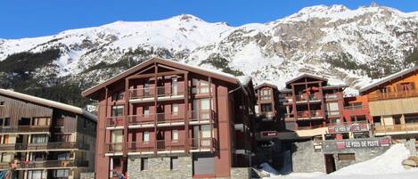 A multi-story building with balconies, a stone facade, and a sign for 'Le Pied de Piste'.