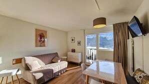 A cozy room with a sofa, a dining table, a TV mounted on the wall, and a window with a view of a snowy landscape. - 300m from ski slopes, 2nd floor, view ski slopes, balcony, tv, ski locker, 25m², Flaine (Flaine)