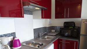 Una cocina con gabinetes rojos, microondas, tostadora, cafetera y lavavajillas.