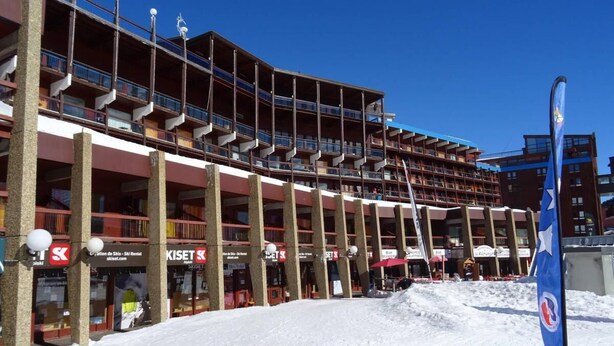 Un edificio de varios pisos con balcones, tiendas de alquiler de esquí y un cartel de estación de esquí.