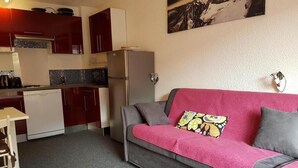 Un espacio habitable compacto con kitchenette, un sofá con un cojín de colores y un cuadro colgado en la pared.