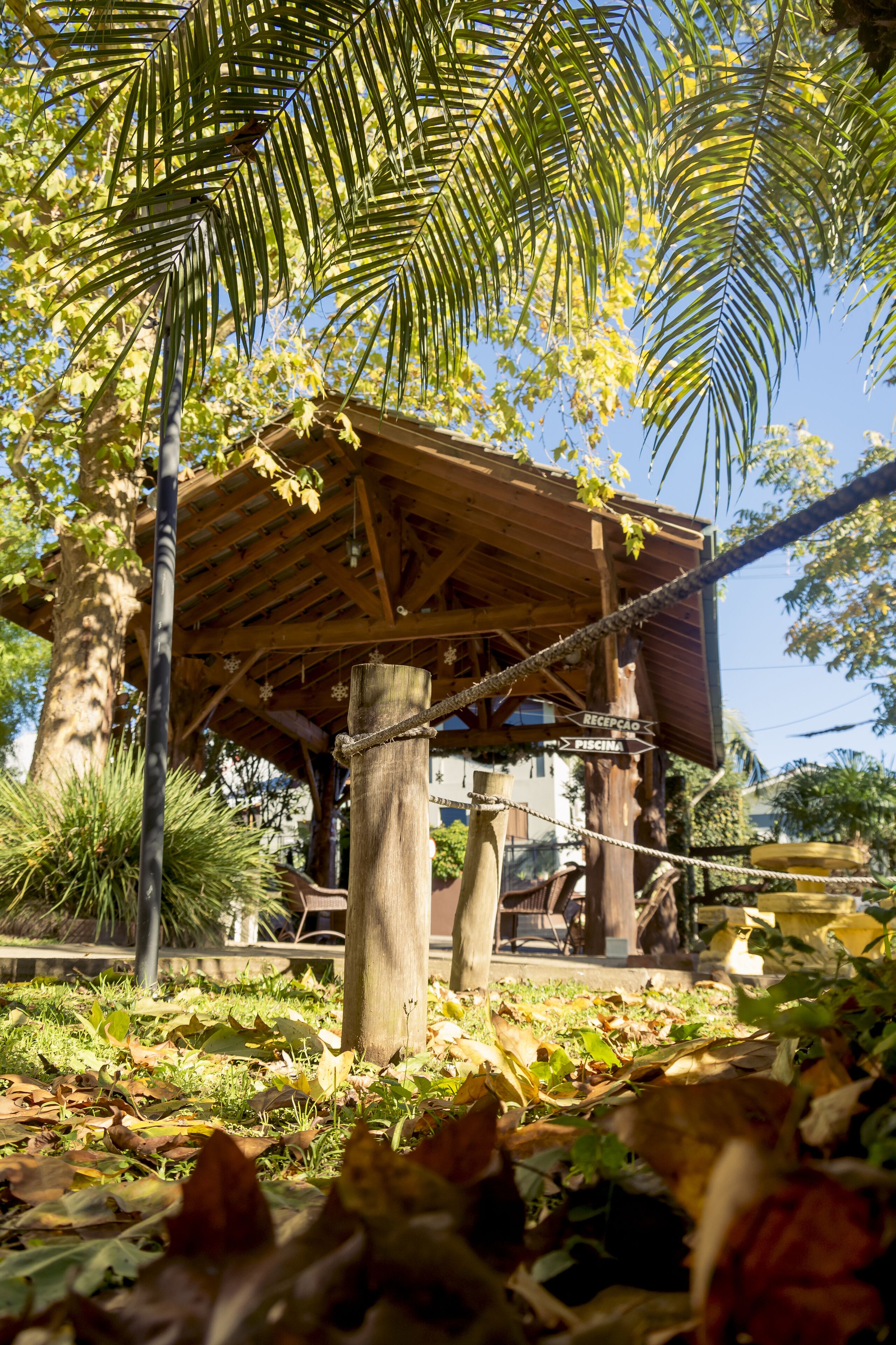 Um gazebo de madeira com uma barreira de corda, cercado por árvores e folhas caídas.