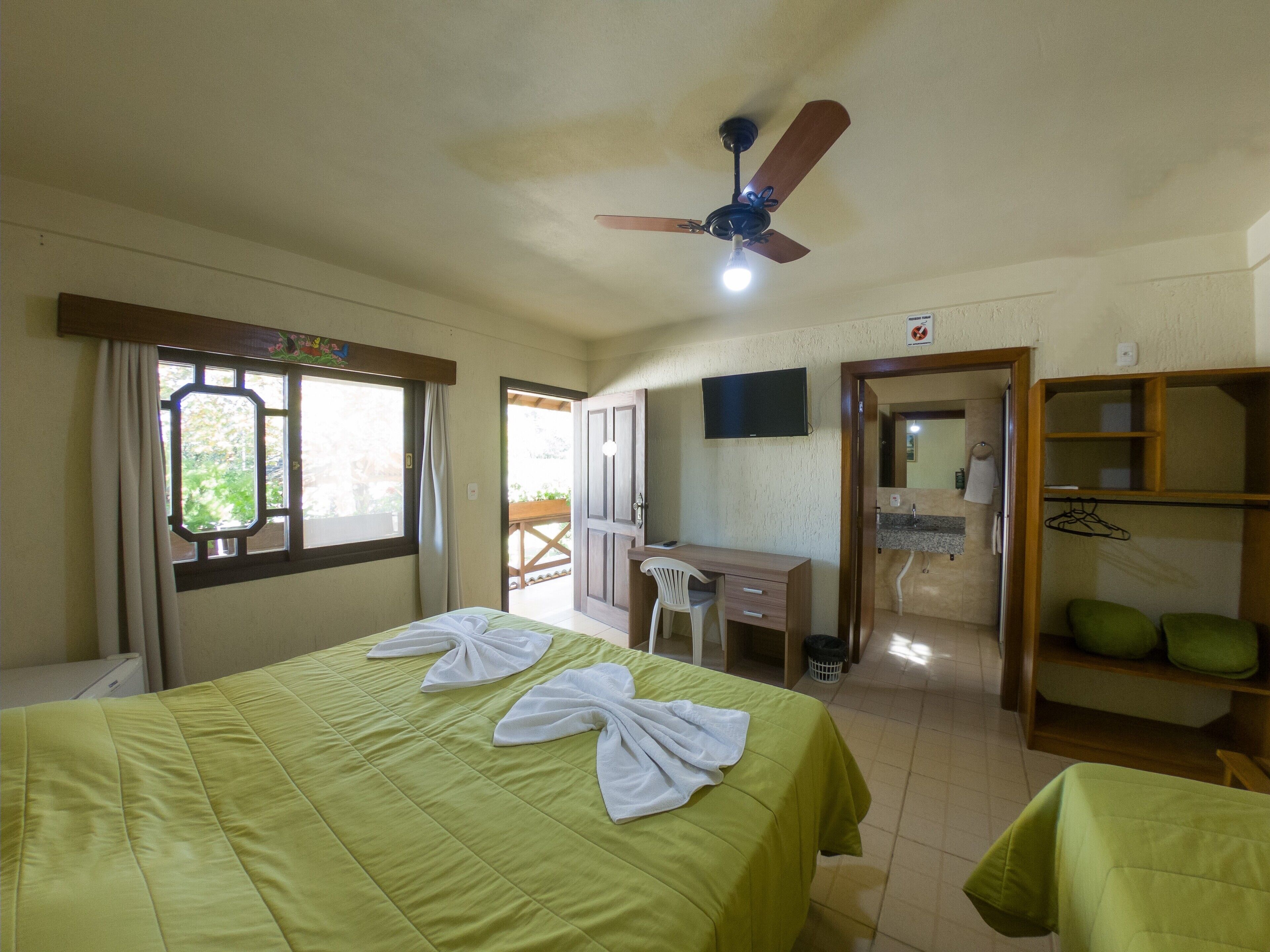 Ein Hotelzimmer mit einem Bett, einem Schreibtisch, einem Stuhl, einem Deckenventilator und einem Fernseher.