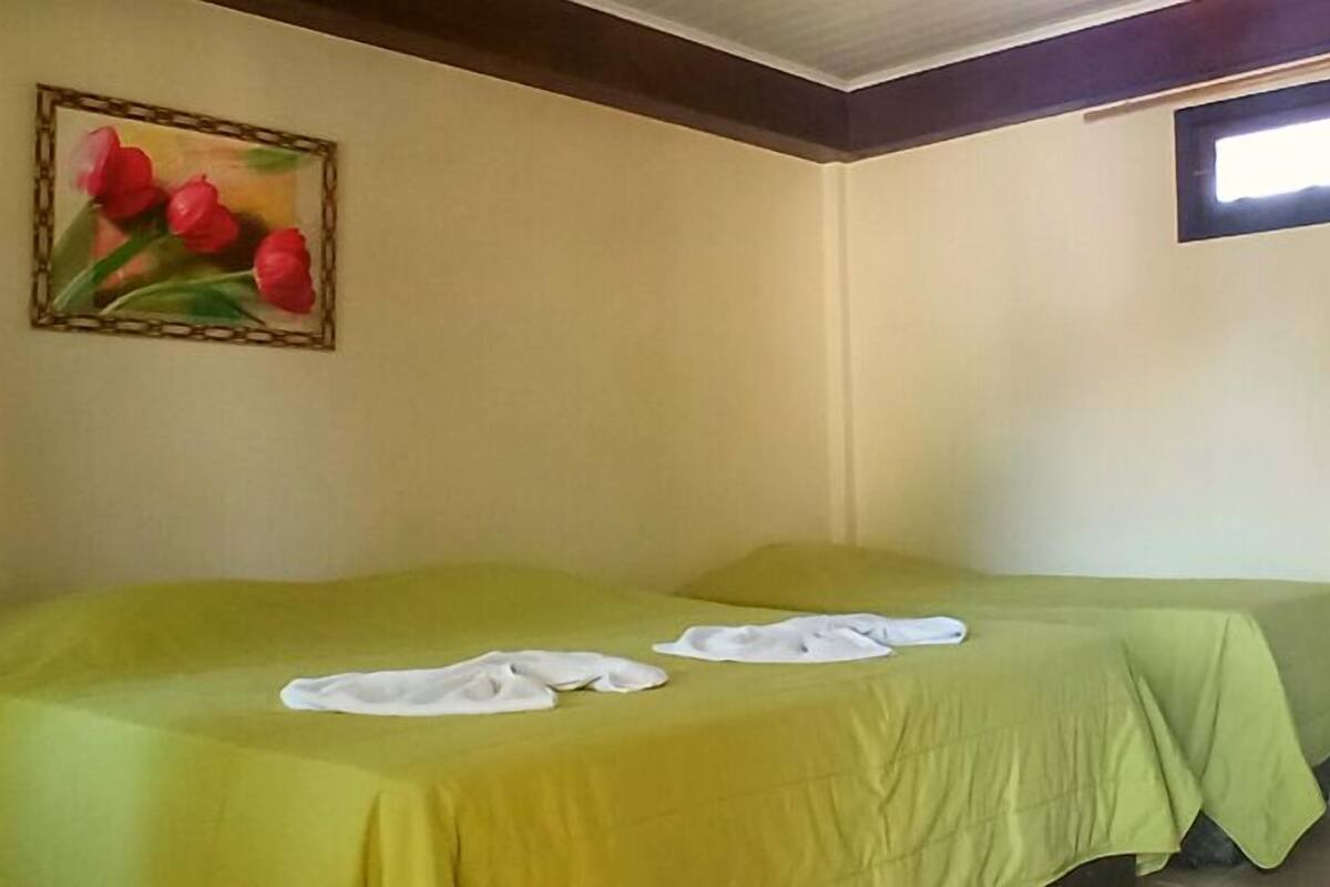 A room with two beds covered in green sheets, a painting of red tulips on the wall, and a window with a view of the sky.