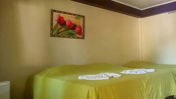 A room with two beds covered in green sheets, a painting of red tulips on the wall, and a window with a view of the sky.