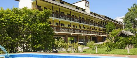 Un hotel con piscina, varios balcones y abundante vegetación.