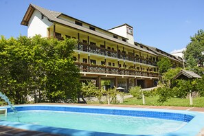 Surrounded by lush greenery, this hotel features a traditional facade with a central balcony and multiple windows.