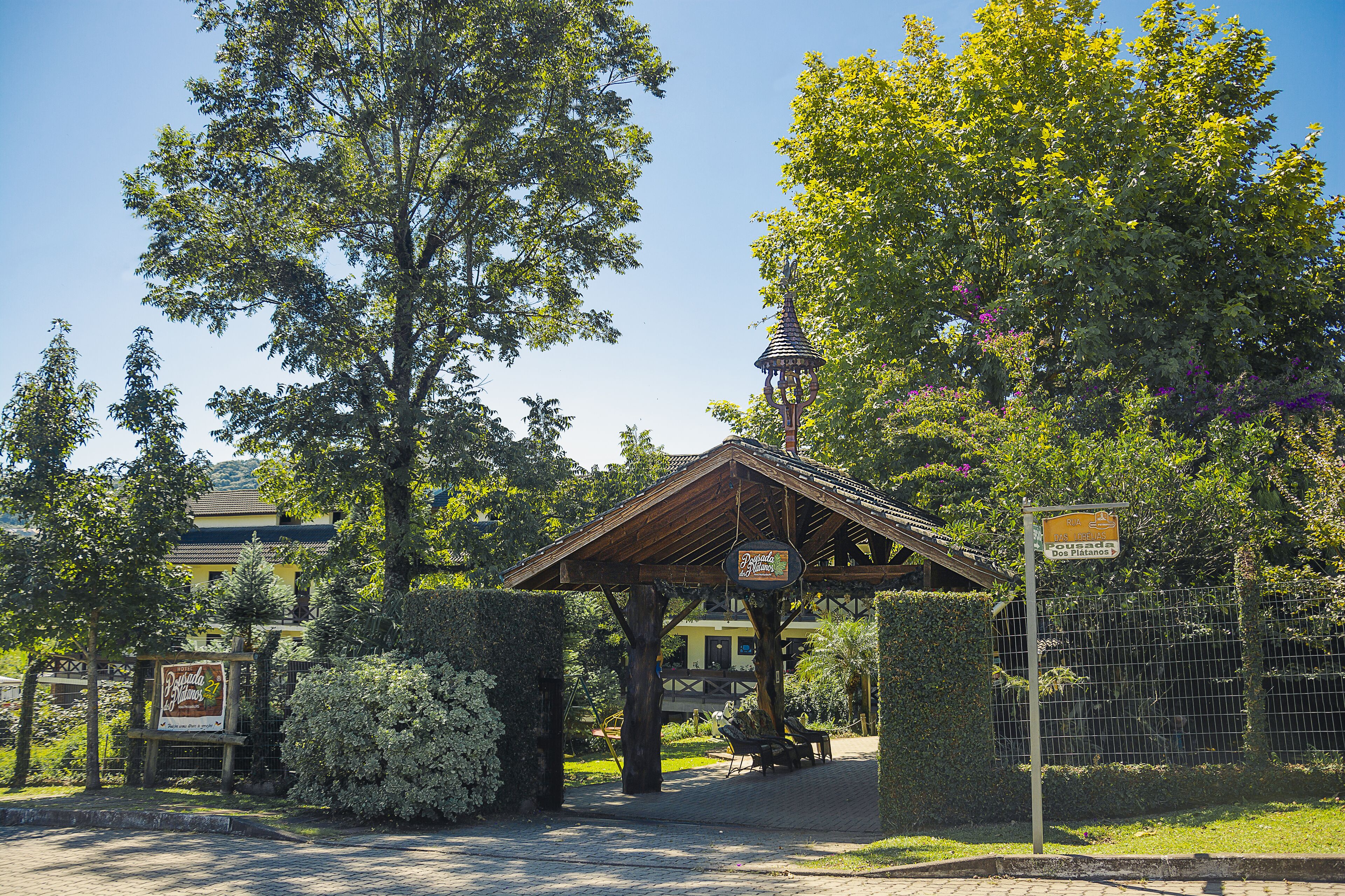 A covered pavilion with a sign, surrounded by lush greenery and a fenced area.