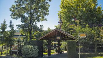 A covered pavilion with a sign, surrounded by lush greenery and a fenced area.