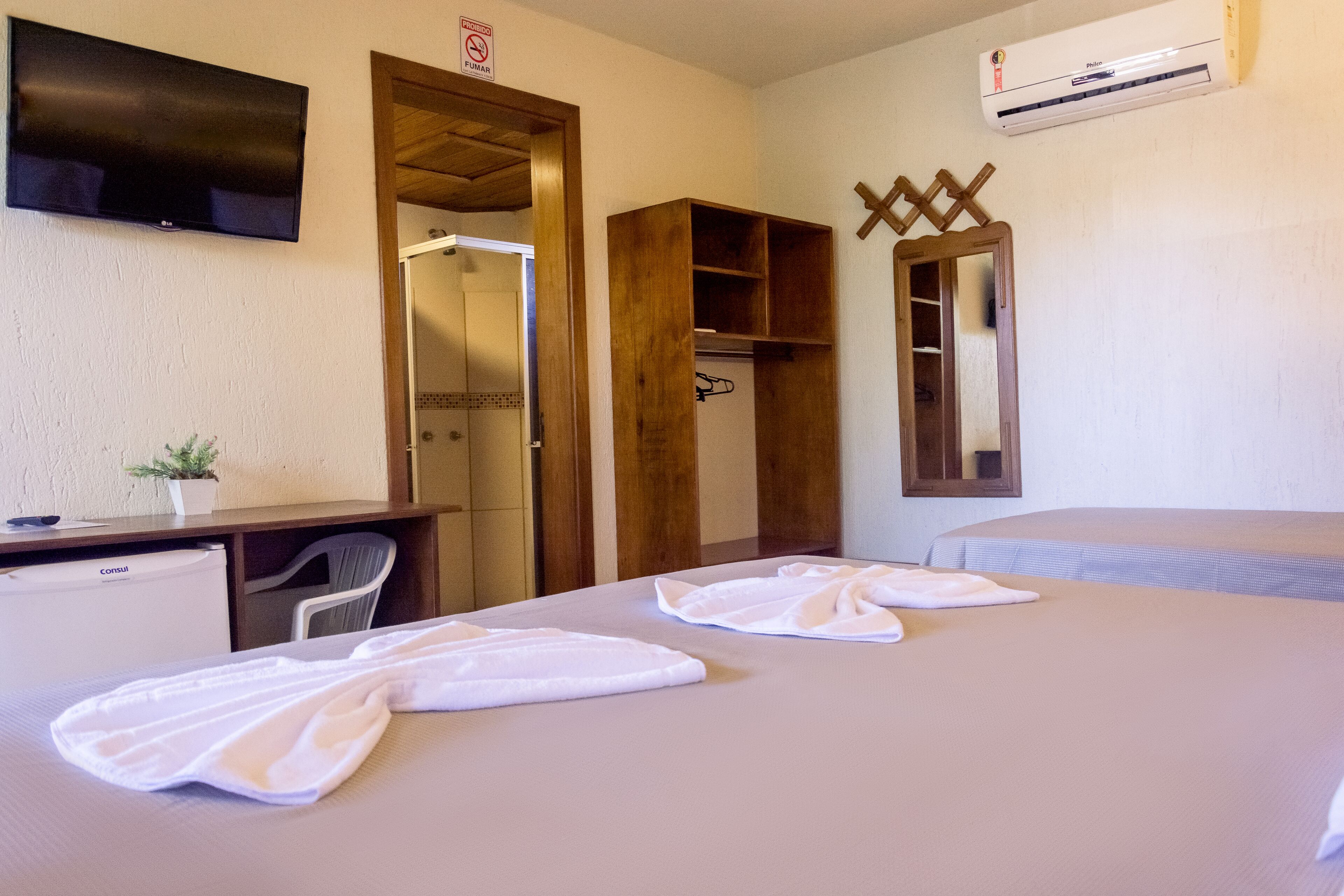 A hotel room with a bed, a desk, a TV, a wardrobe, and an air conditioning unit.