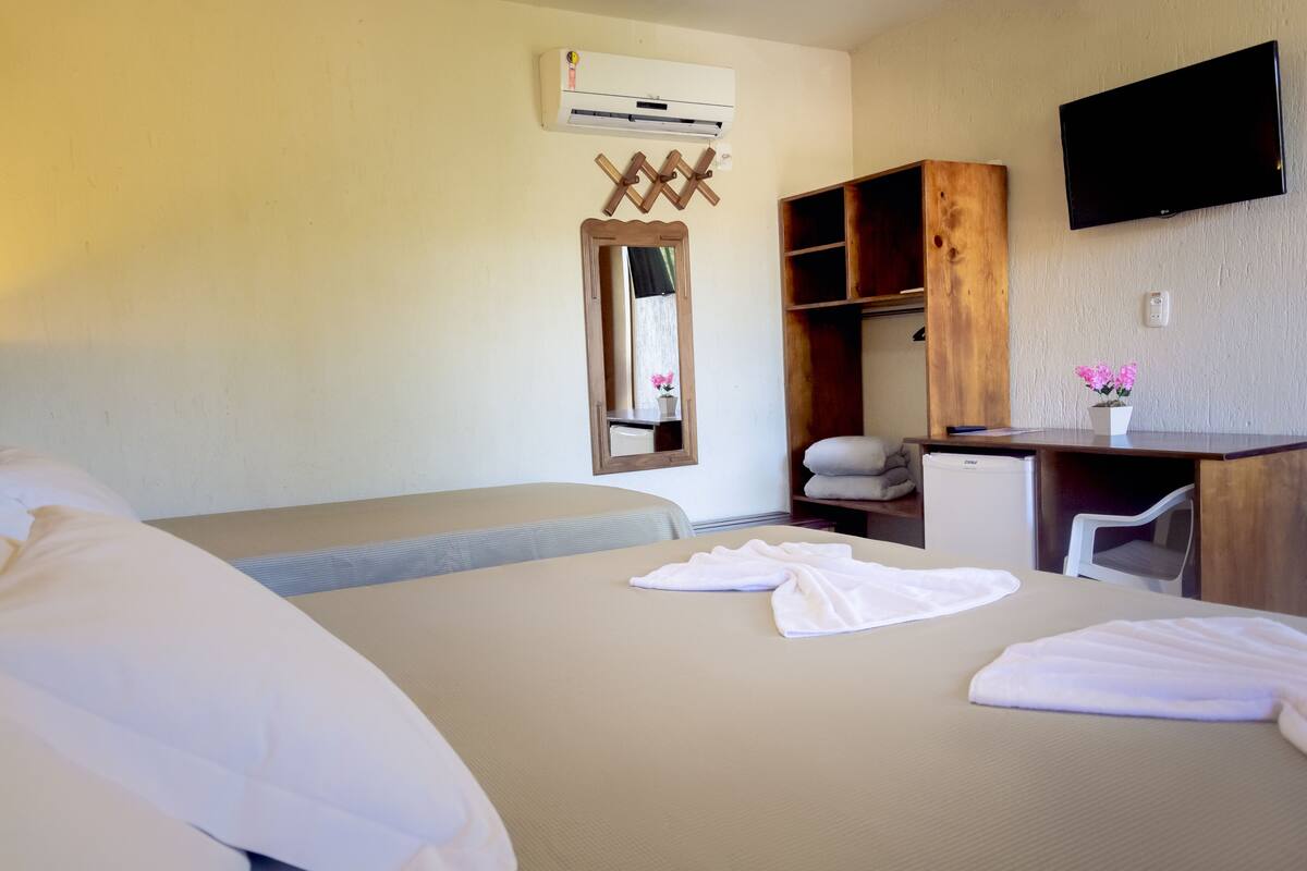 A hotel room with a bed, a desk, a chair, a TV, and a mirror.