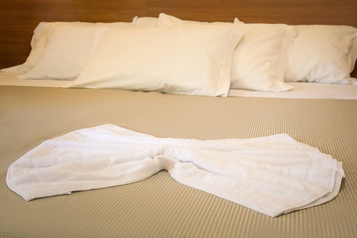 A neatly made bed with white linens and a white bathrobe on it, a painting on the wall, and a wooden headboard.