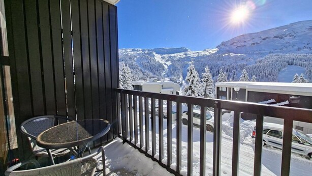 Een balkon met een tafel en stoelen, met uitzicht op een besneeuwd berglandschap onder een heldere lucht.