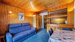 Een knus blokhutinterieur met een blauwe bank, houten wanden en een eethoek met een tafel.