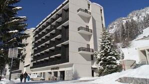 Een hotel met meerdere verdiepingen, met een modern architectuurontwerp, voorzien van balkons op elke verdieping en een besneeerd landschap op de achtergrond.
