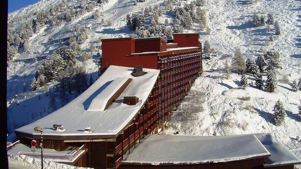 Et hotel med en lang, rød bygning med mange vinduer, beliggende på en snedækket bjergskråning.