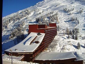 Un hotel con un lungo edificio rosso e numerose finestre, situato su un pendio montuoso innevato.