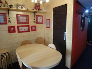 A wooden interior with a round table and chairs, framed pictures on the wall, and a door with a handle.