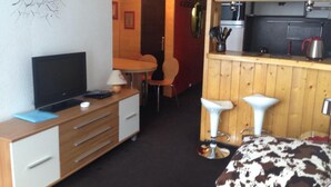Et kompakt hotelværelse med et træskrivebord, et fjernsyn, et lille tekøkken og en seng med mønstret sengetæppe.