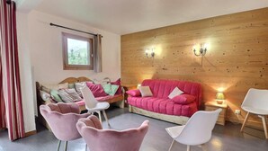 Ett mysigt rum med en väggpanel av trä, en röd soffa, två rosa fåtöljer och en vit stol.