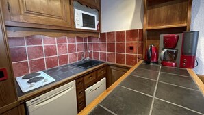 A compact kitchen with wooden cabinets, a microwave, a sink, a dishwasher, and a coffee maker. - 20m from shops, 4th floor, view street, balcony, tv, ski locker, 25m², Les Menuires (Les Menuires)