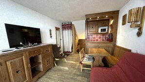 A compact living space with a wooden kitchenette, a dining area, a television, and a red sofa. - 20m from shops, 4th floor, view street, balcony, tv, ski locker, 25m², Les Menuires (Les Menuires)