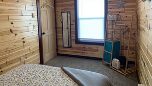 Une pièce aux murs en bois, un lit recouvert d’une couvre-lit à motifs floraux, une fenêtre avec des stores, une décoration en forme d’étoile et un meuble de rangement bleu.
