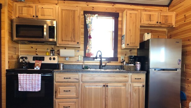 Une cuisine avec des meubles de rangement en bois, un four à micro-ondes en acier inoxydable, une cuisinière, un réfrigérateur et une fenêtre avec un rideau.