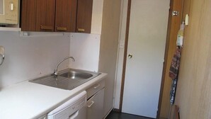 A compact kitchen with a sink, a dishwasher, wooden cabinets, and a white door.