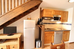A compact kitchen with wooden cabinets, a refrigerator, a microwave, and a sink.