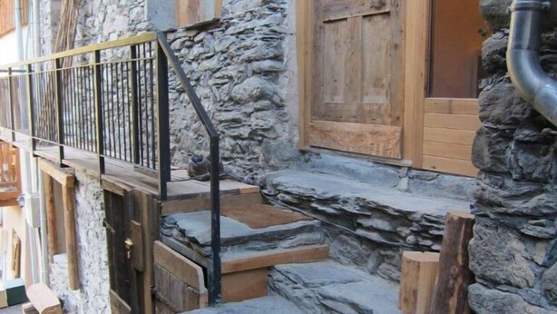 A stone building with a wooden staircase and a metal railing.