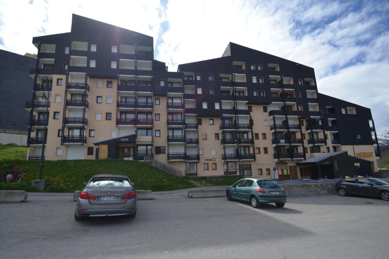 Un edificio residenziale a più piani con balconi, un'area di parcheggio e un piccolo edificio d'ingresso.