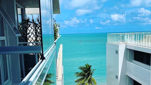 Ein modernes Hotel mit Poolbereich, Palmen und Blick auf den Strand.