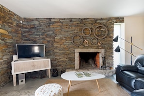A living room with a stone wall, a fireplace, a television on a wooden cabinet, a black leather sofa, and a white coffee table.