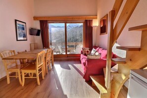 A room with a wooden dining table and chairs, a red sofa, and a large window with a mountain view.