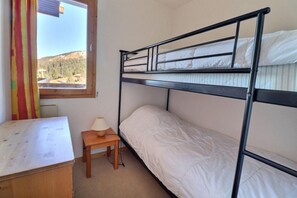 A bunk bed room with a window, a small wooden table, and a lamp.