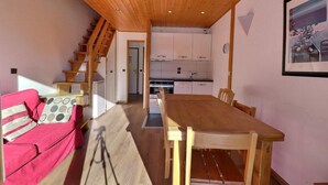 Ett mysigt rum med ett träpanelat tak, ett matbord, en rosa soffa och en trappa som leder upp till ett köksområde.