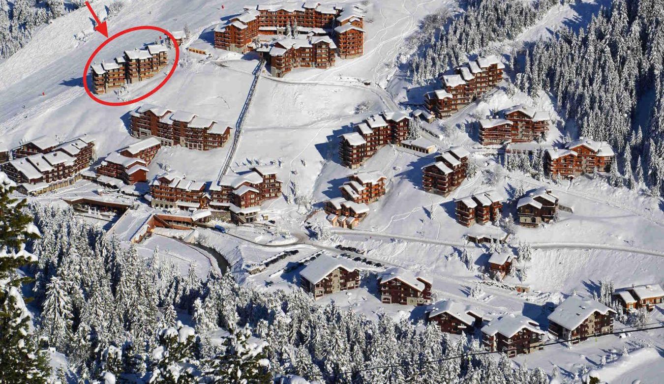 A snow-covered resort with multiple chalet-style buildings, ski slopes, and a dense forest in the background.