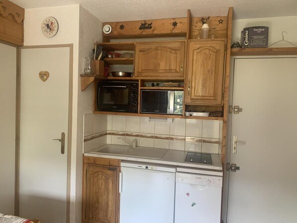A compact kitchen with wooden cabinets, a microwave, a dishwasher, and a small countertop.