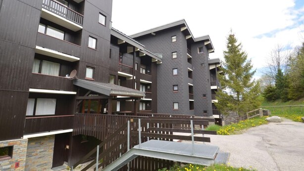 A multi-story building with balconies, a stone facade, and a paved area with a bench. - 300m from shops, 3rd floor, view mountain, balcony, tv, ski locker, 25m², Les Menuires (Les Menuires)