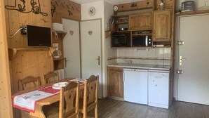 A compact kitchen with wooden cabinets, a microwave, a dishwasher, and a dining table with chairs. - 300m from shops, 3rd floor, view mountain, balcony, tv, ski locker, 25m², Les Menuires (Les Menuires)