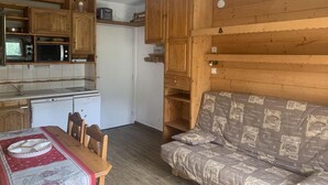 A compact kitchen with wooden cabinets, a microwave, and a refrigerator. There is a dining table with chairs and a patterned sofa. - 300m from shops, 3rd floor, view mountain, balcony, tv, ski locker, 25m², Les Menuires (Les Menuires)